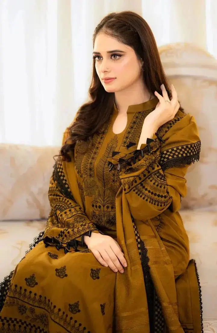 Woman wearing a mustard yellow traditional outfit with black embroidery in an indoor setting.