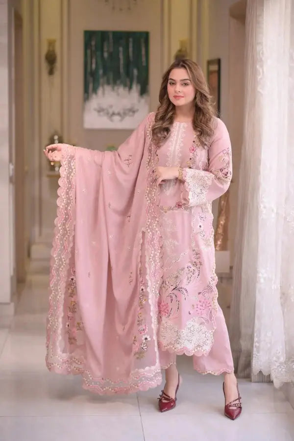 Woman in a pink embroidered outfit standing in a decorated room.